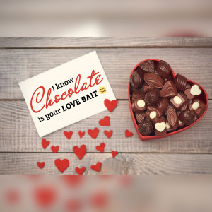 A heart-shaped box of chocolates and a card that says 'I know chocolate is your love bait'