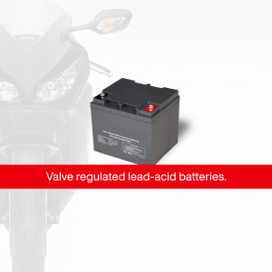 Close-up of a black motorcycle battery with red and black terminals, positioned in front of a blurred motorcycle.