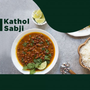 Close-up of Kathol Sabji, a lentil-based dish, served in a white bowl with rice and lime wedges.