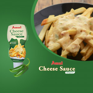 Close-up of French fries covered in Amul Cheese Sauce with a bottle of sauce and a jalapeno pepper.