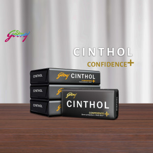 Three Cinthol Confidence+ soap bars stacked on a wooden surface with packaging.