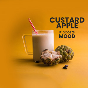 A glass of custard apple smoothie with a custard apple fruit and seeds on a yellow background.
