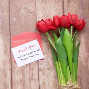 A bouquet of red tulips and a thank you card on a wooden surface.