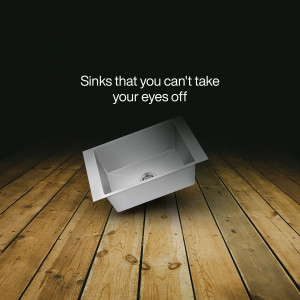 A sleek, stainless steel kitchen sink on a wooden floor with dramatic lighting.