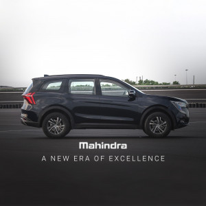Side view of a dark blue Mahindra XUV700 with the Mahindra logo and tagline.