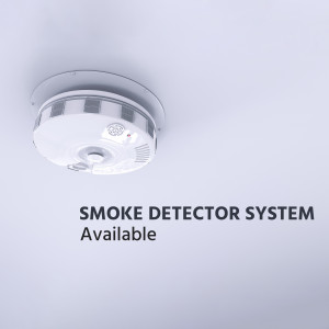 Close-up of a white smoke detector mounted on a light blue wall with text 'SMOKE DETECTOR SYSTEM Available'