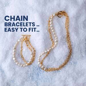 Close-up of layered gold and pearl chain bracelets on a textured white surface.