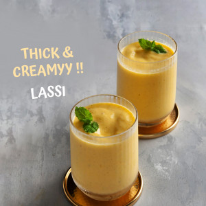 Two glasses of mango lassi garnished with mint leaves on a textured surface.