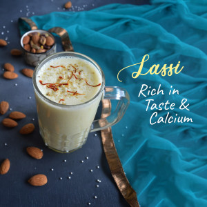 A glass of creamy lassi garnished with saffron and surrounded by almonds.