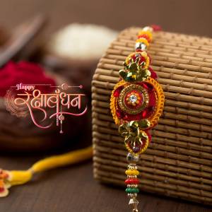 Close-up of a colorful Rakhi bracelet on a woven surface with Raksha Bandhan greetings.