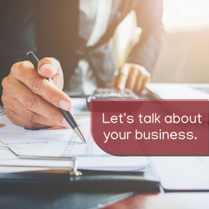 Man writing on documents with a pen, financial charts and calculator visible, with text 'Let's talk about your business.'