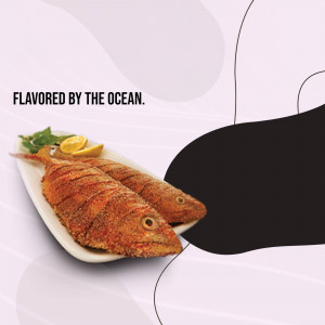 Close-up of two fried fish served with lemon and greens on a white plate.