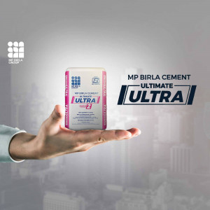 A hand holding a bag of MP Birla Cement Ultimate against a blurred city background.