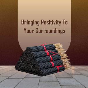 A stack of black incense sticks tied with red ribbon on a tiled surface with text 'Bringing Positivity To Your Surroundings'