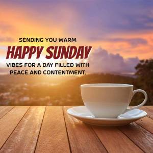 A cup of coffee on a wooden table with a sunset background and the text 'Happy Sunday'