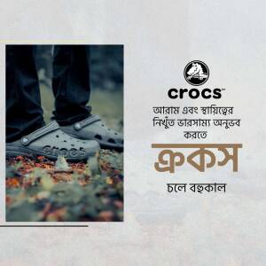 A person wearing grey Crocs shoes standing on autumn leaves with the Crocs logo and Bengali text.