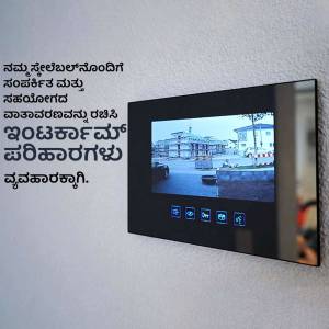 A wall-mounted smart video doorbell displaying a live camera feed with Kannada text on the screen.