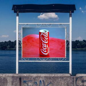 A Coca-Cola can displayed within a billboard frame overlooking a river.