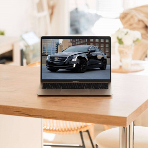 Laptop displaying a black Cadillac car on a wooden table