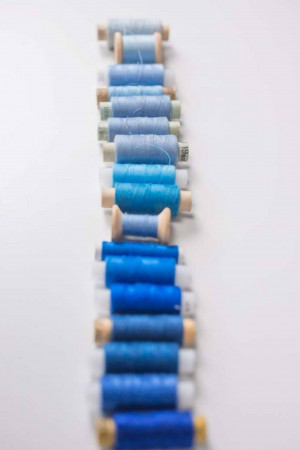 A vertical line of spools of thread in various shades of blue.