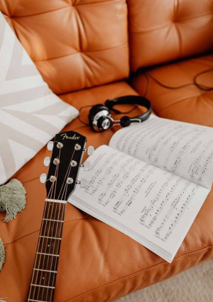 A guitar, headphones, and sheet music on an orange leather couch.