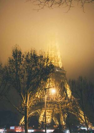 The Eiffel Tower illuminated at night, partially obscured by fog.