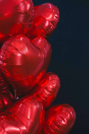 Close-up of a cluster of shiny red heart-shaped balloons against a dark background.