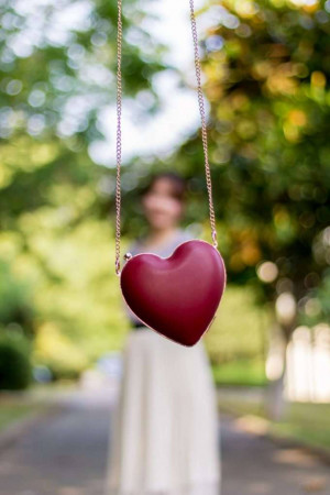 Red heart-shaped handbag hanging in front of a blurred woman in a garden