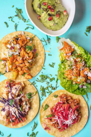 Overhead shot of colorful tacos with various fillings on a bright blue background.