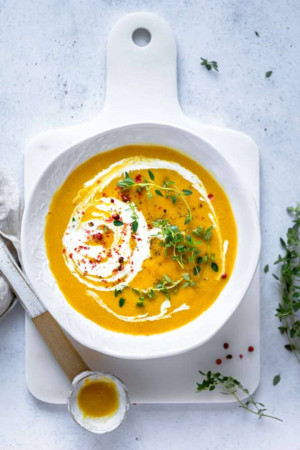 Overhead shot of butternut squash soup in a white bowl with a swirl of cream and herbs.