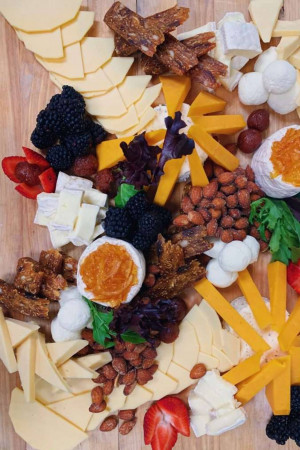A beautifully arranged cheese and charcuterie board with various cheeses, fruits, nuts, and meats.