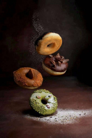 A visually appealing image of assorted donuts in mid-air with powdered sugar.