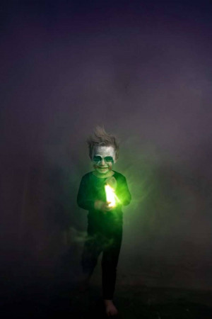A young child with face paint holding a glowing light stick in a smoky environment.