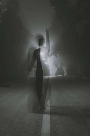 A blurred, ghostly figure standing on a dark road at night.