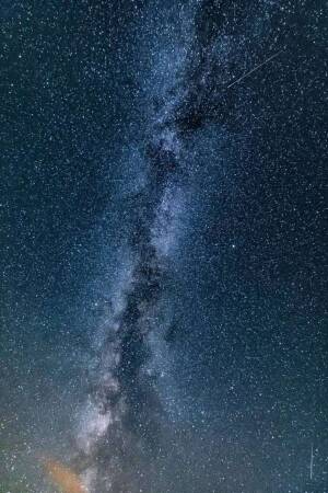 A stunning vertical view of the Milky Way galaxy stretching across a dark night sky with a shooting star.