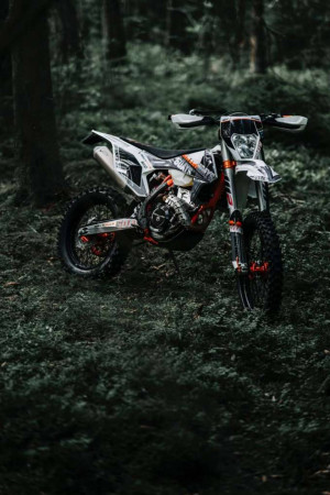 Orange and white dirt bike parked in a lush green forest