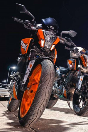 Close-up of an orange and black KTM Duke motorcycle with a helmet on the seat, parked at night.