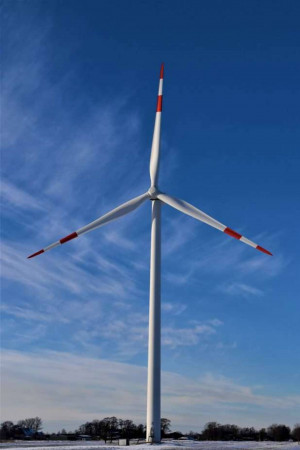 A tall white wind turbine with red tips on its blades against a clear blue sky.
