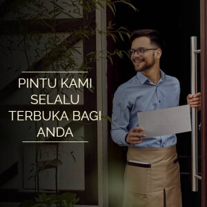 A man standing in a doorway holding a blank sign with text in Indonesian.