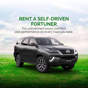 Gray Toyota Fortuner parked in a green field with text promoting self-drive rentals.