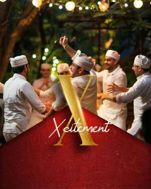 Group of men in traditional Omani dress celebrating with a large golden 'X' in the foreground.