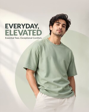 A young man wearing a sage green oversized t-shirt with the text Everyday Elevated