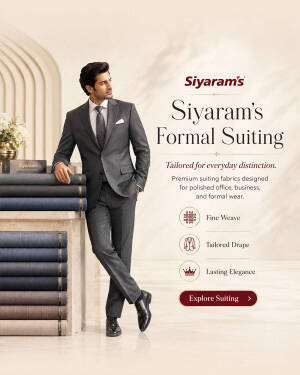 A man in a grey Siyaram's formal suit standing next to a stack of fabric rolls.