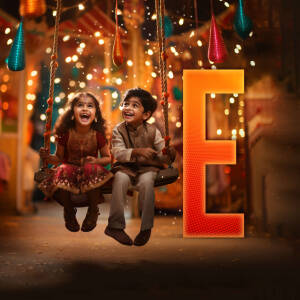 Two children enjoying a swing during a Diwali festival with a large illuminated 'E' in the background.