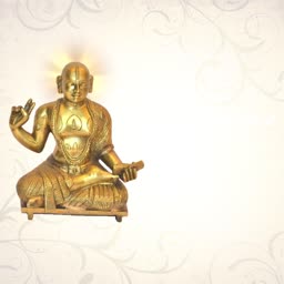 A golden brass statue of the philosopher Ramanujacharya seated in a meditative posture against a soft patterned background.