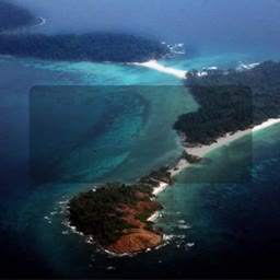 An aerial shot of a narrow tropical island land bridge connecting two larger land masses surrounded by turquoise water