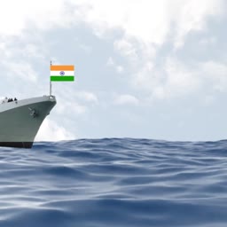 A view of the bow of an Indian naval warship sailing on a calm ocean with the Indian flag flying.