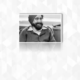 A smiling man wearing a turban and sweater, shown in a black and white portrait style with a geometric patterned background.