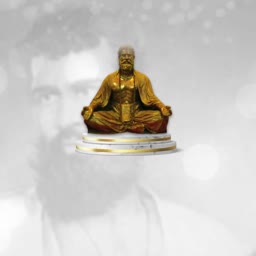 A gold-colored statue of a meditating saint positioned on a pedestal against a faint, bokeh-effect background of a man.