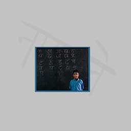 A young Indian boy standing in front of a chalkboard featuring Devanagari script characters in a classroom setting
